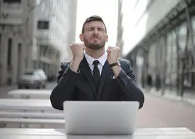 Uomo in giacca e cravatta che alza i pugni simbolo di successo personale e mindset vincente